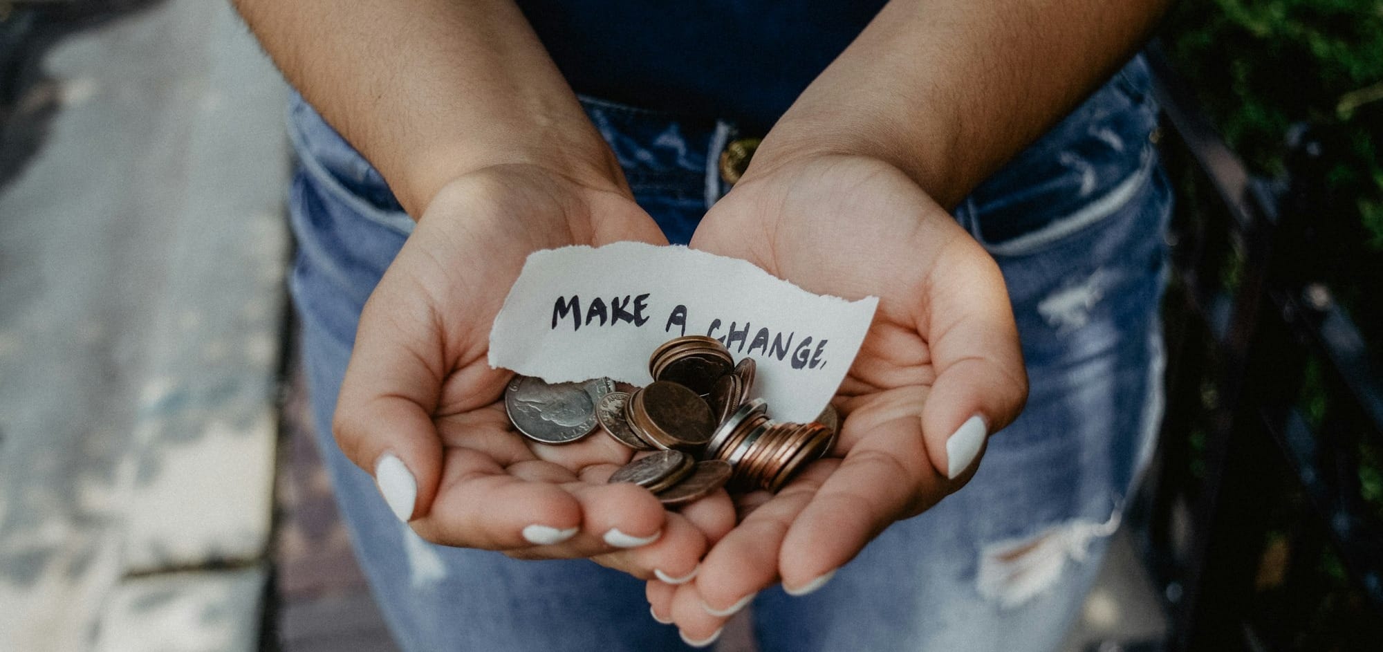 Cupped hands holding coins and a torn paper note reading 'make a change'