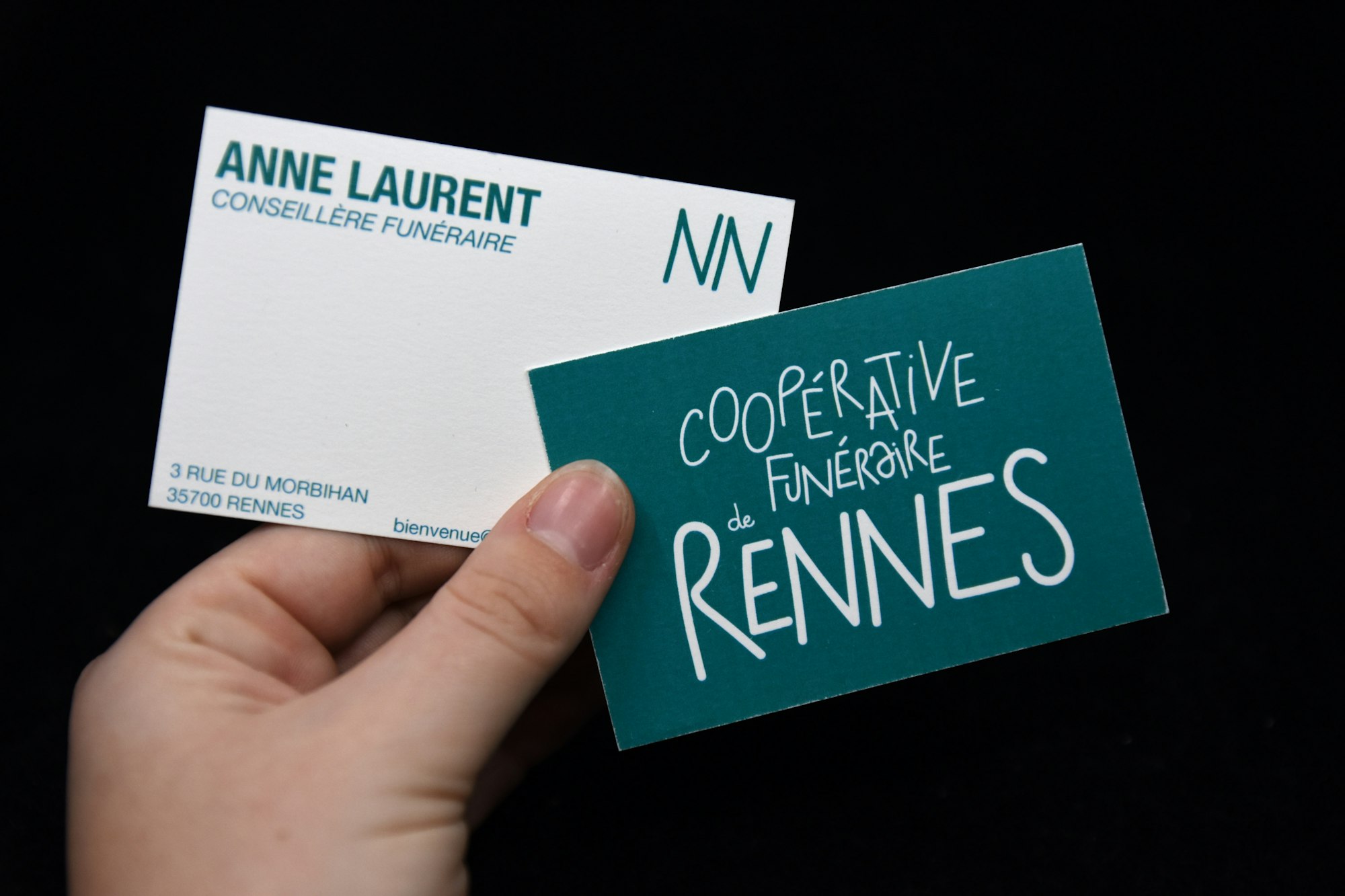 Hand holding two business cards against a black background
