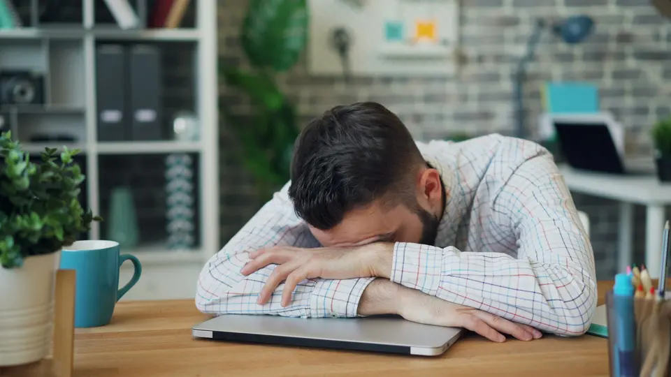 Person resting their head on folded arms beside an open notebook
