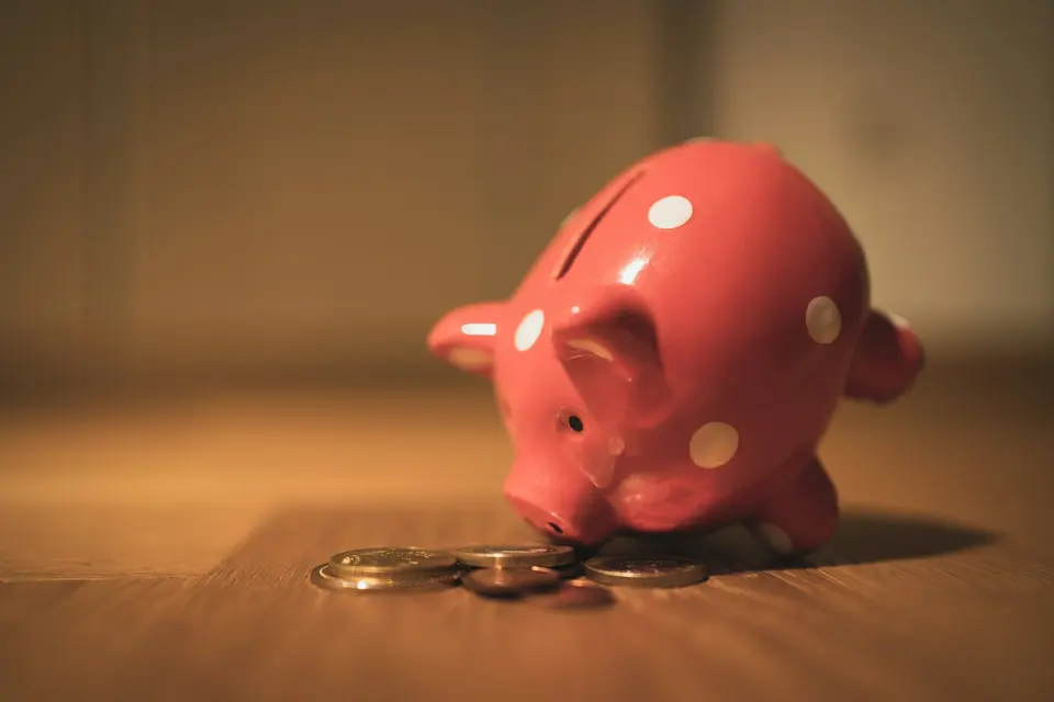 A pink piggy bank beside coins on a wooden surface