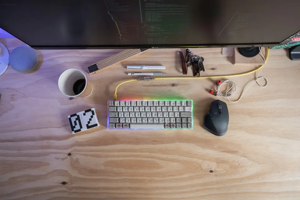 An overhead view of a keyboard, mouse, monitor, and coffee on a wooden desk