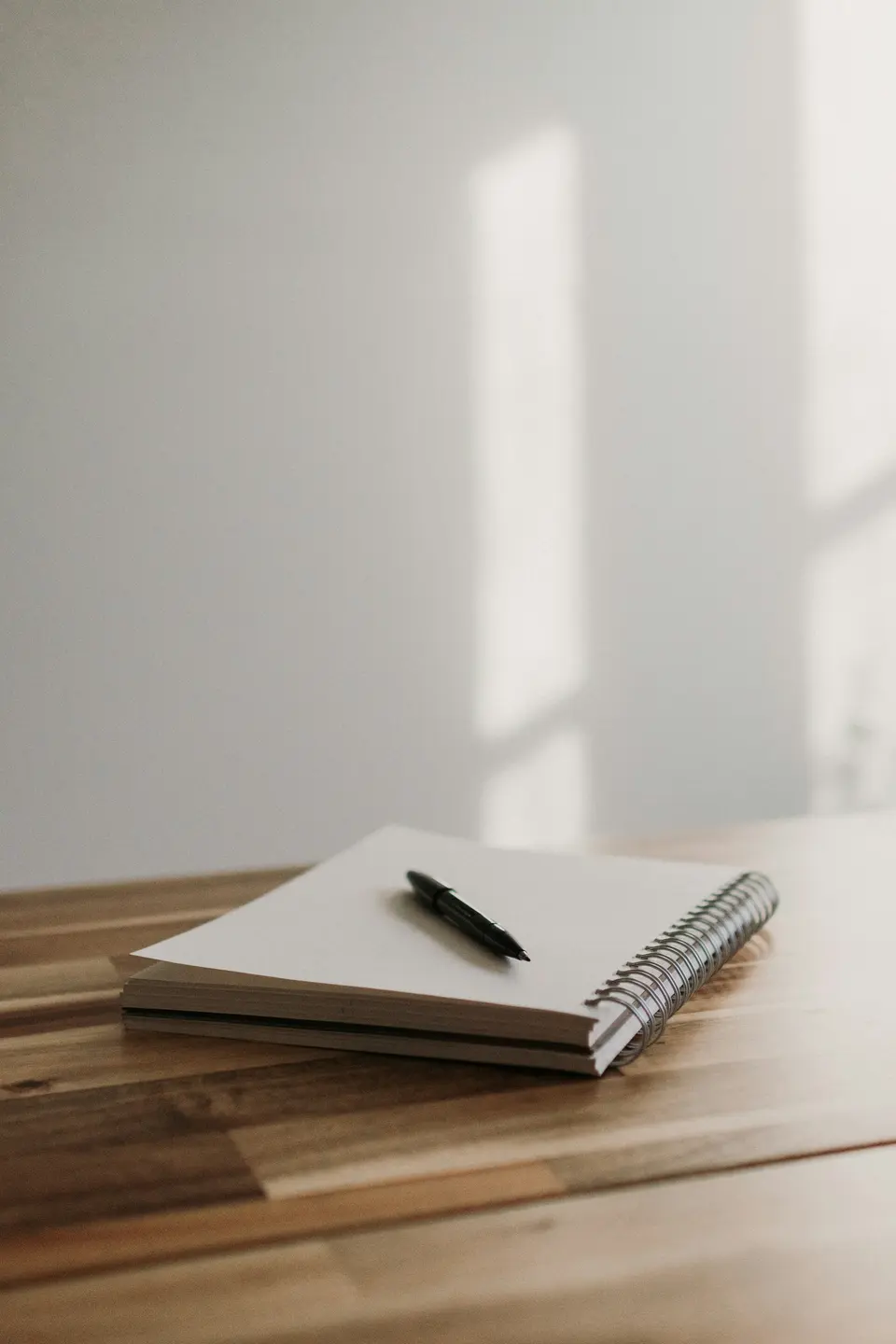A notebook with a pen on top of a wooden table