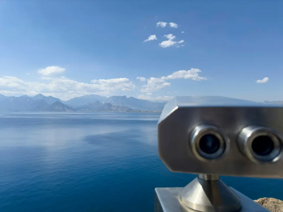 Viewing binoculars overlooking blue water and distant mountains