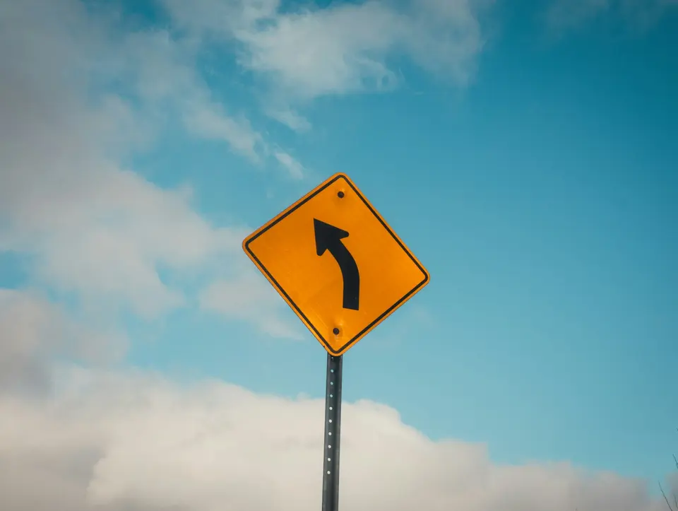A yellow road sign showing a left curve beneath a blue sky