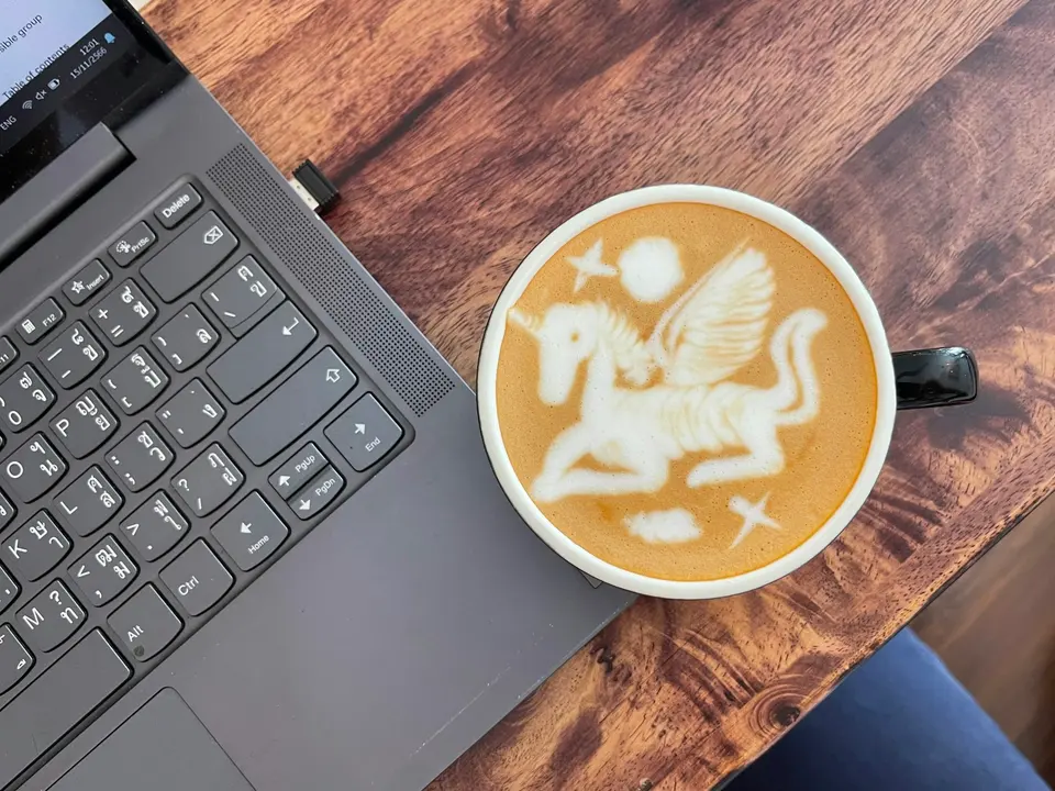 A cup with latte art beside a laptop on a wooden table