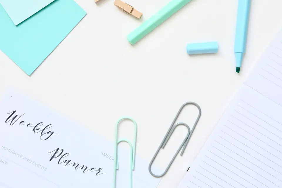A weekly planner beside paper clips and pastel markers