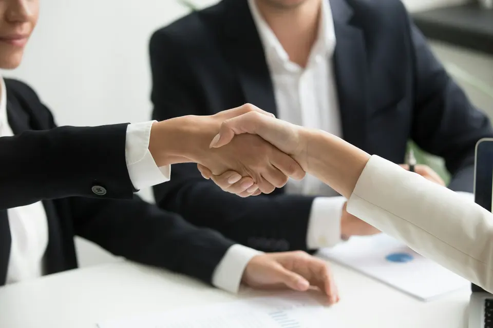 Two people shaking hands in front of a laptop