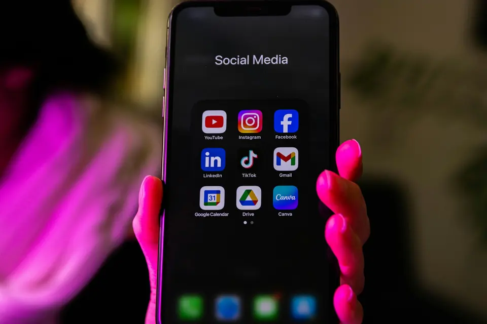 A hand holding a smartphone displaying a folder of app icons