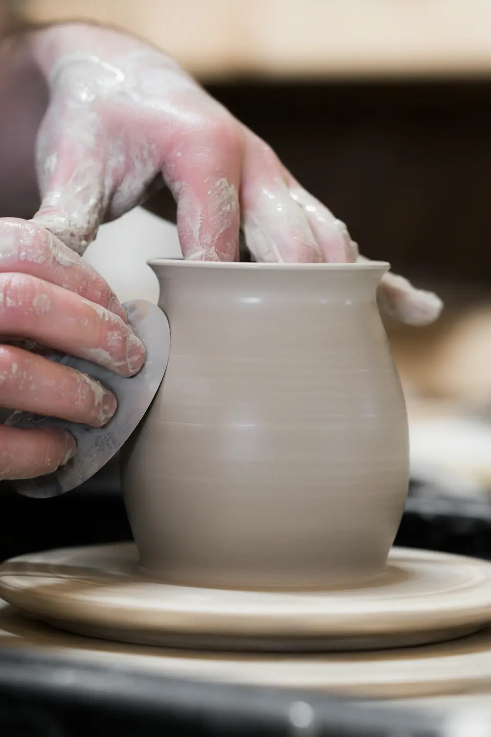 A person's hands holding a finished white clay pot