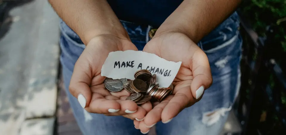 Cupped hands holding coins and a paper note reading make a change