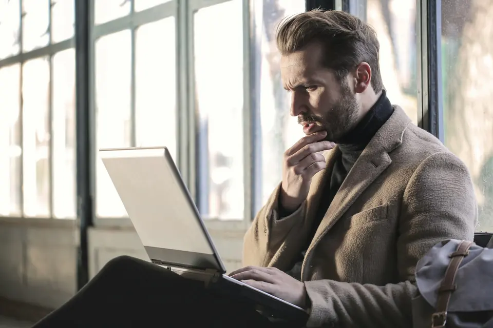 A person seated with a laptop beside tall windows